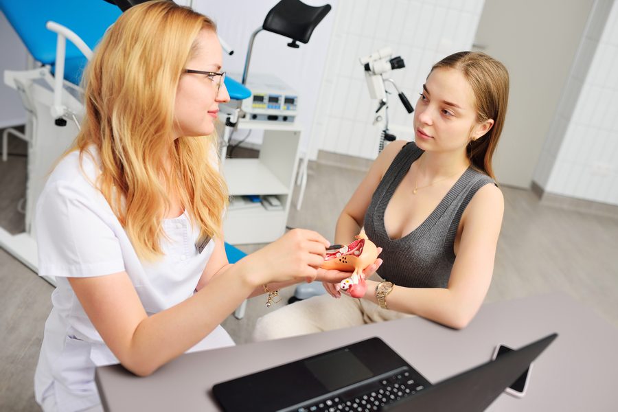 a young attractive girl at a women's consultation with a gynecologist. The gynecologist shows the patient a model of the uterus and talks about women's health against the background of a gynecological chair.