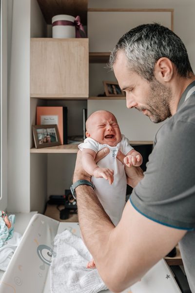 A vertical shot of a Caucasian dad holding his crying baby, and getting ready to change diapers.