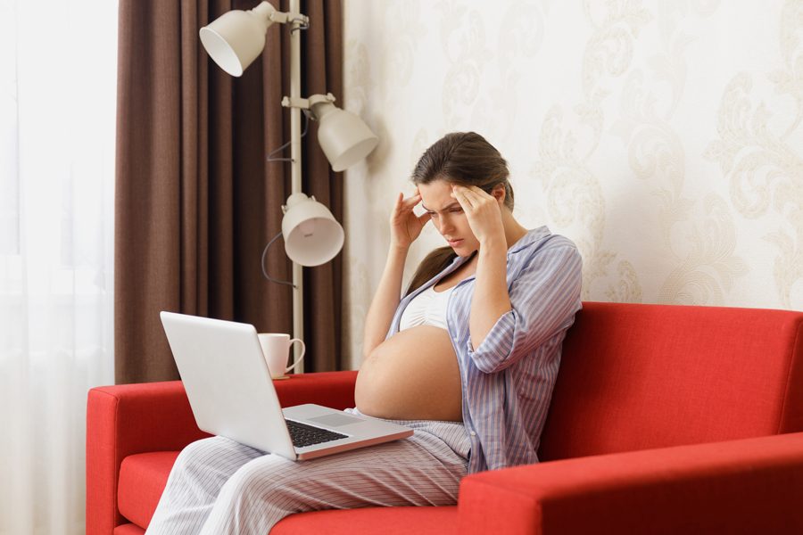 Tired pregnant woman sitting with a laptop computer on the red sofa