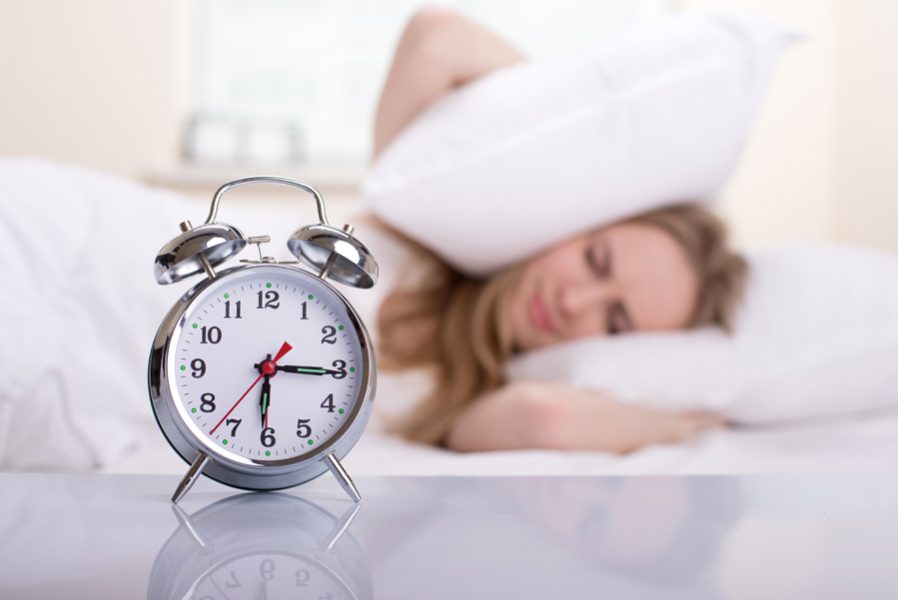 Young woman with alarmclock on the bed at the morning.